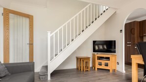 Een moderne woonkamer met een trap, een grijze bank, een tv op een houten standaard en een houten kast.
