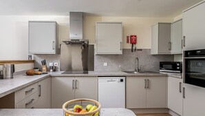 Een moderne keuken met witte kastjes, roestvrijstalen apparatuur en een fruitschaal op het aanrecht.