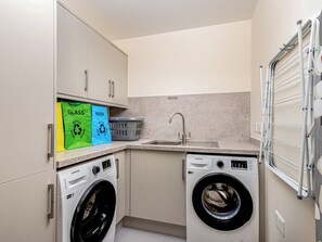 A compact laundry room with two front-loading washing machines, a sink, and a drying rack. - Durham Lodge - UKC5799 (Lundin Links)