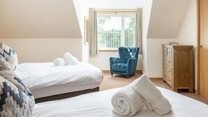 Un dormitorio con dos camas, un sillón azul, un aparador de madera y una ventana con cortinas.