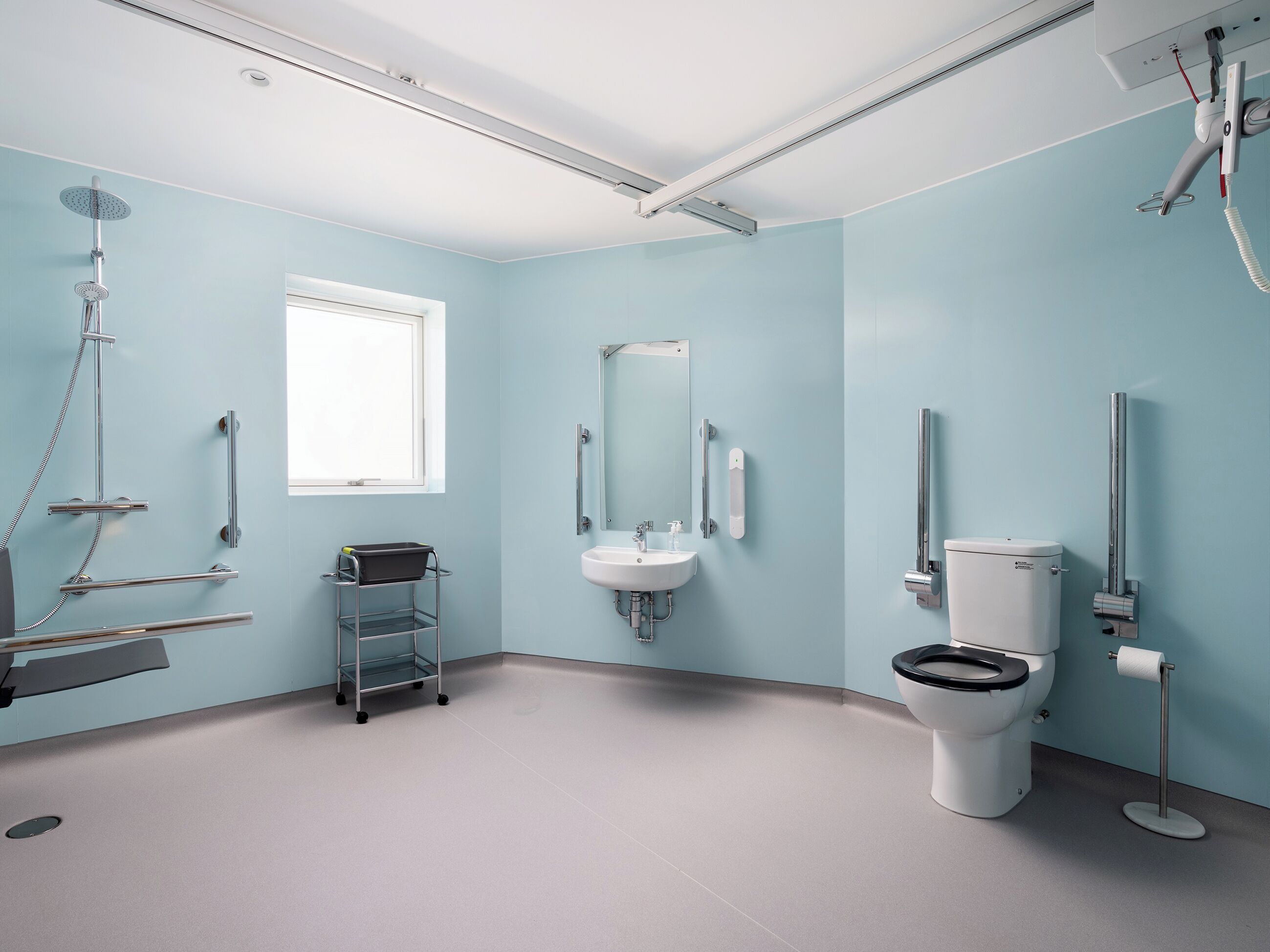 A modern bathroom with a shower, toilet, and sink, featuring a light blue wall and a window.