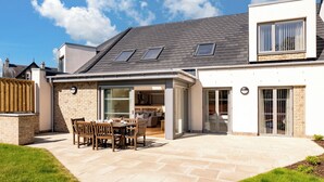 A modern house with a patio, a dining area, and a kitchen visible through glass doors. - Largo Lodge - UKC5801 (Lundin Links)