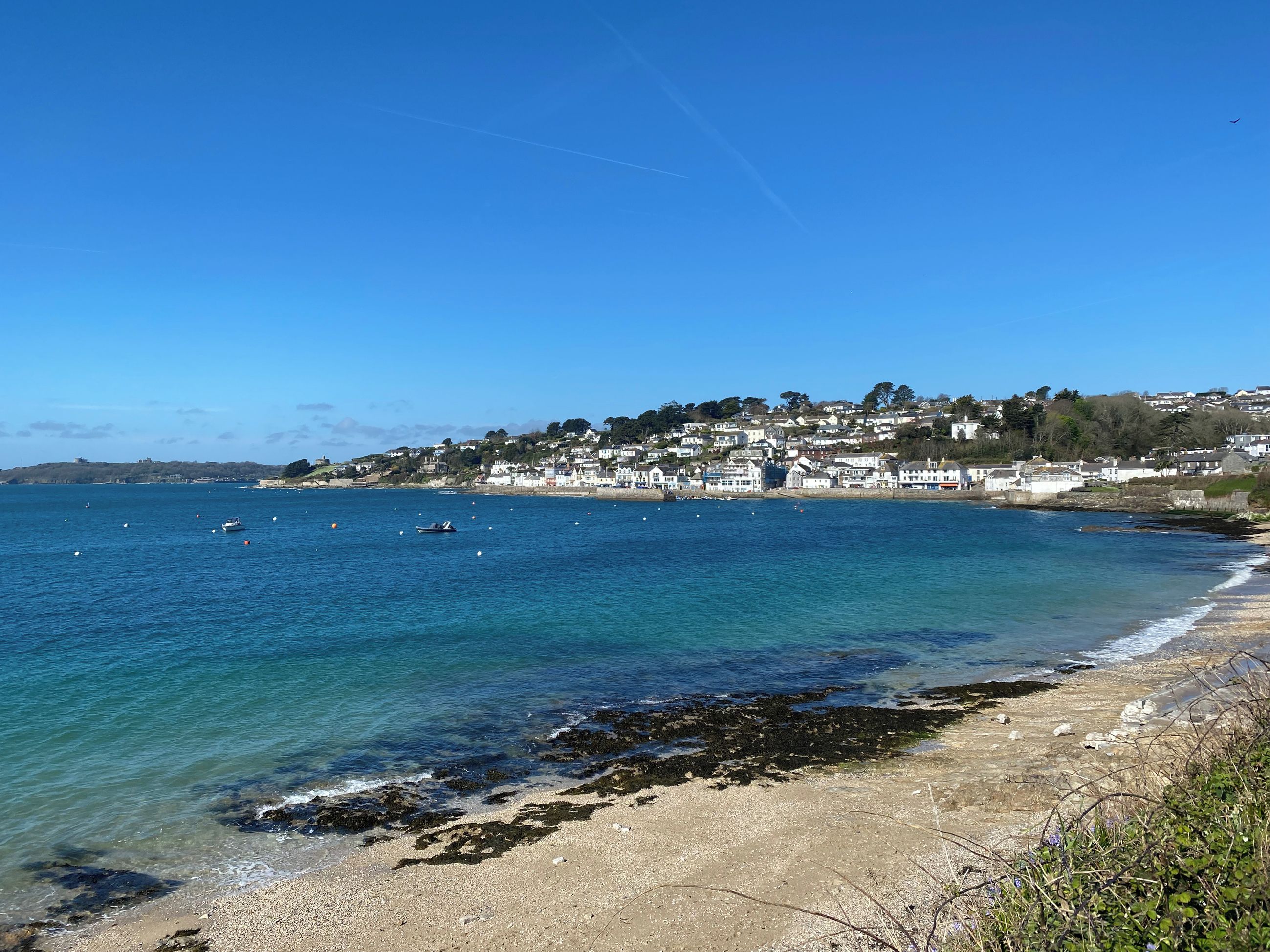 Une ville côtière où le ciel est d’un bleu éclatant, la mer est calme et la plage est sablonneuse, parsemée d’algues.