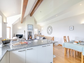 A spacious living area with a fireplace, a dining table set for four, and a large clock on the wall. - 2 bedroom accommodation in St Just in Roseland, near Truro (St Just in Roseland, near Truro)