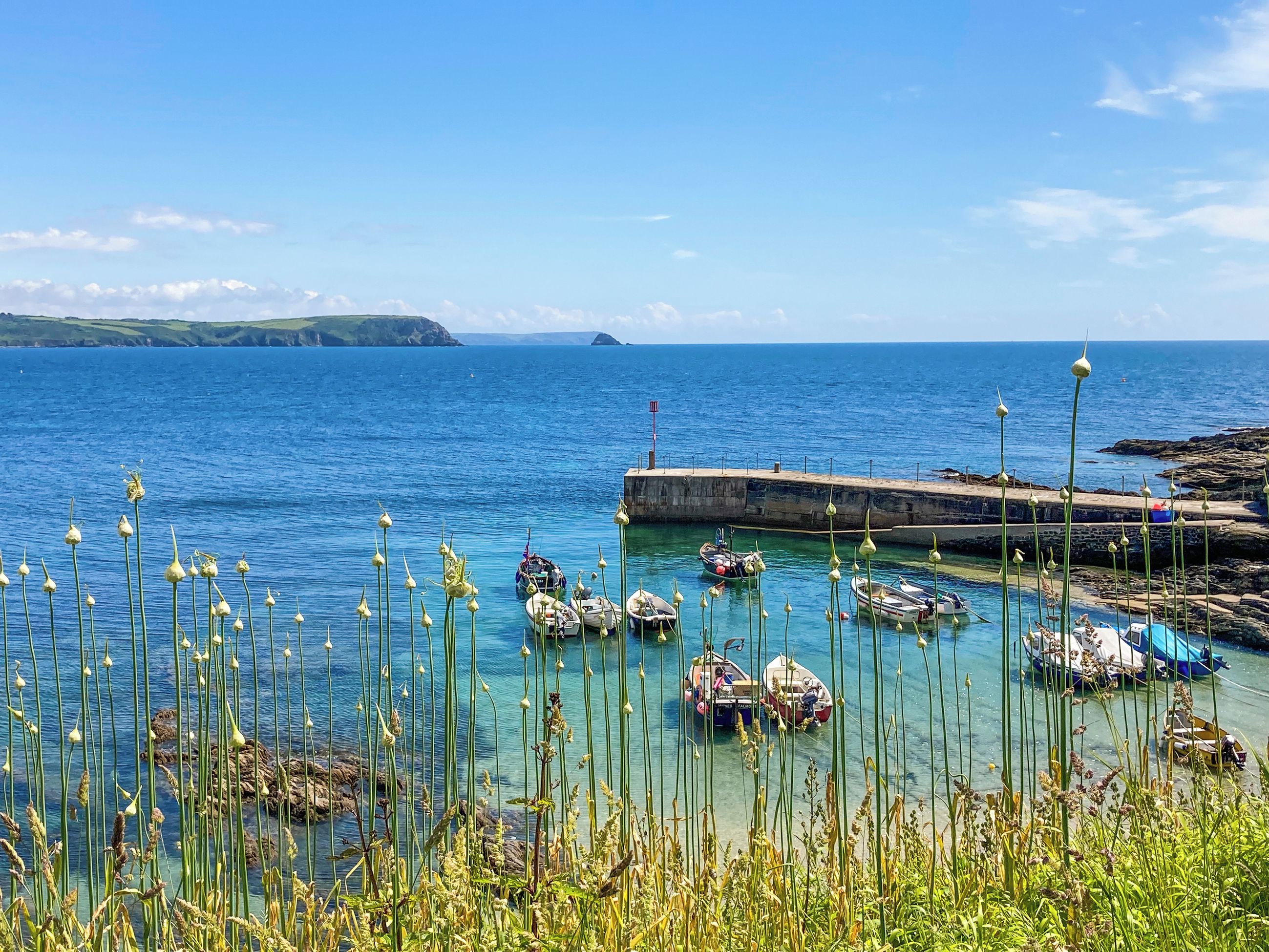 Un paysage côtier avec des bateaux amarrés à un quai, une eau claire et une côte rocheuse.