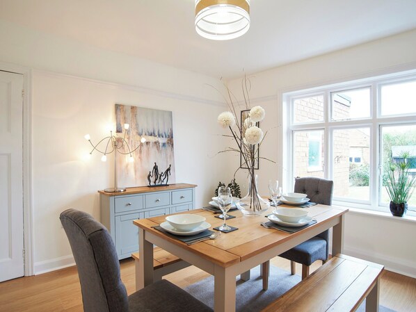 A dining area with a wooden table set for two, a vase with white flowers, and a painting on the wall.