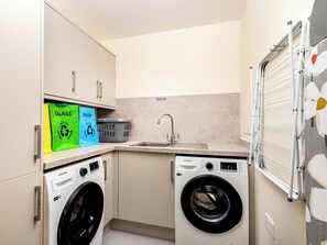 A compact laundry room with two Samsung washing machines, a sink, and a drying rack. - Selkirk Lodge - UKC5803 (Lundin Links)