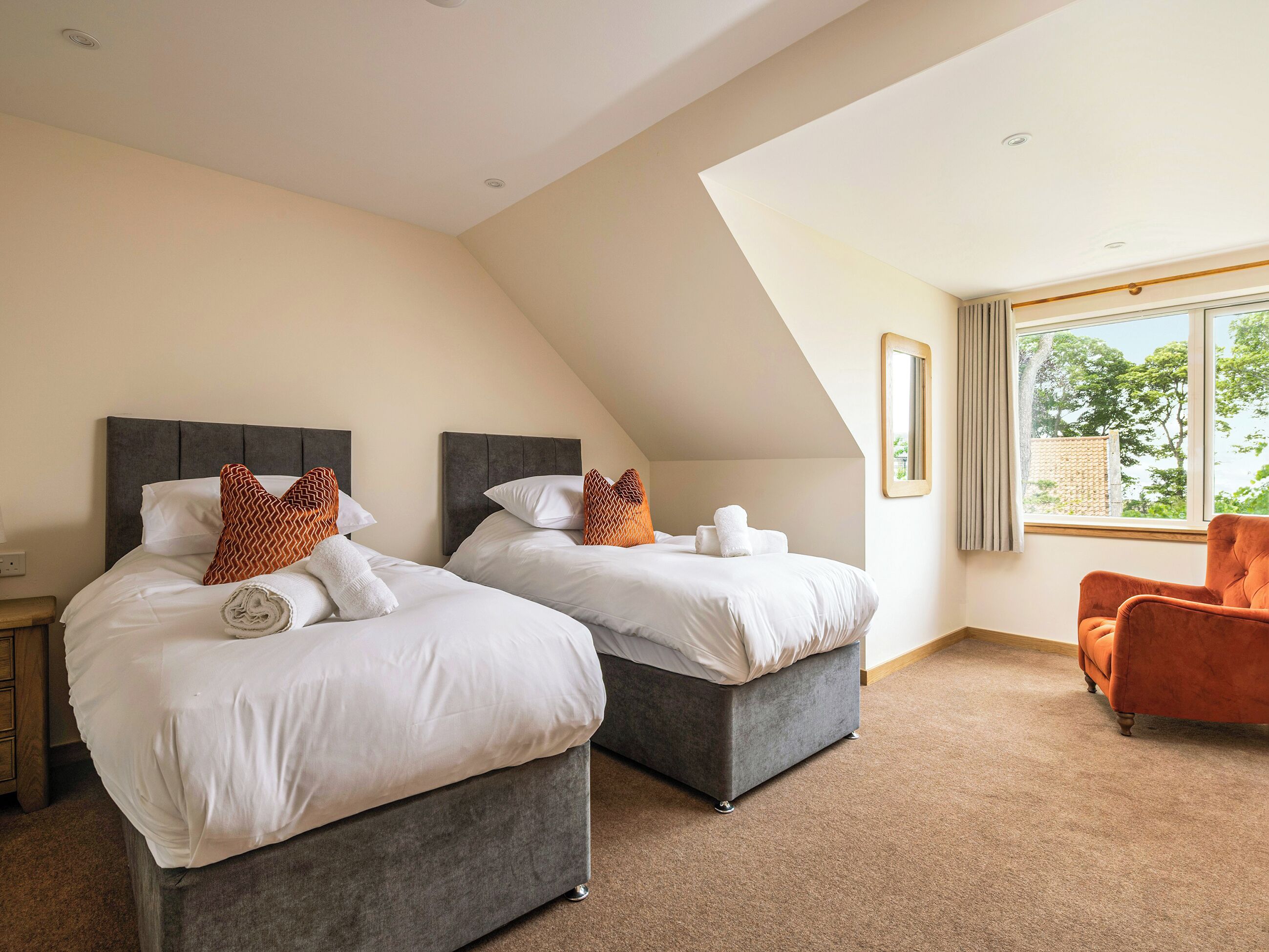 A hotel room with two beds, a large window with a view, and an orange chair.