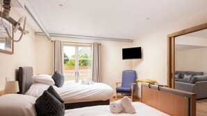 Ein Hotelzimmer mit zwei Betten, einem Fernseher, einem Sessel und Blick ins Freie.