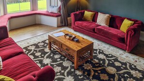 Un salón con sofá rojo, una mesa de centro de madera y un banco junto a la ventana con vistas a un paisaje verde.
