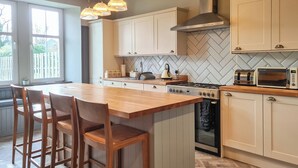 Una cocina moderna con una isla central, taburetes de madera, estufa a gas, microondas y un salpicadero con patrón de espiga.