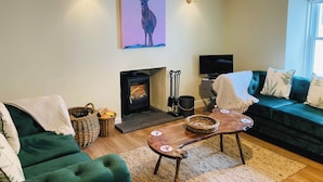 Ein gemütliches Wohnzimmer mit Kamin, einem grünen Sofa und einem Bild von einem Reh.
