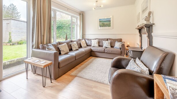 A spacious living room with a large L-shaped sofa, a wooden coffee table, and a fireplace. - Hollyhocks is a charming cottage that is over 100 years old. (St Minver, near Rock)