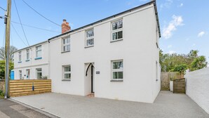 A two-story building with a white exterior, a wooden fence, and a small garden area. - Hollyhocks is a charming cottage that is over 100 years old. (St Minver, near Rock)