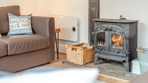 A cozy living room with a brown sofa, a decorative pillow, a vintage-style fireplace, and a wicker basket. - Hollyhocks is a charming cottage that is over 100 years old. (St Minver, near Rock)