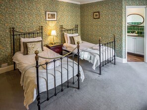 A double bed with a metal frame, a nightstand, a lamp, and a wall with floral wallpaper. - 7 bedroom accommodation in Sedgeford, near Hunstanton (Sedgeford, near Hunstanton)