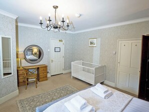 Une chambre à coucher avec un berceau, une table de chevet, un miroir, un lustre et une porte ornée d’un tableau.