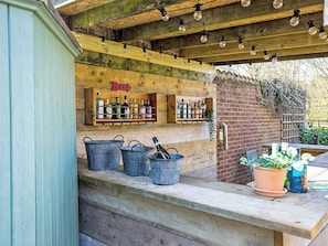 A rustic outdoor bar with wooden beams, hanging light bulbs, and shelves of bottles. - 7 bedroom accommodation in Sedgeford, near Hunstanton (Sedgeford, near Hunstanton)