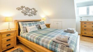 Ein Schlafzimmer mit einem hölzernen Bett, Karo-Bettwäsche, Nachttischen mit Lampen, einer Kommode und einer Wanddekoration.