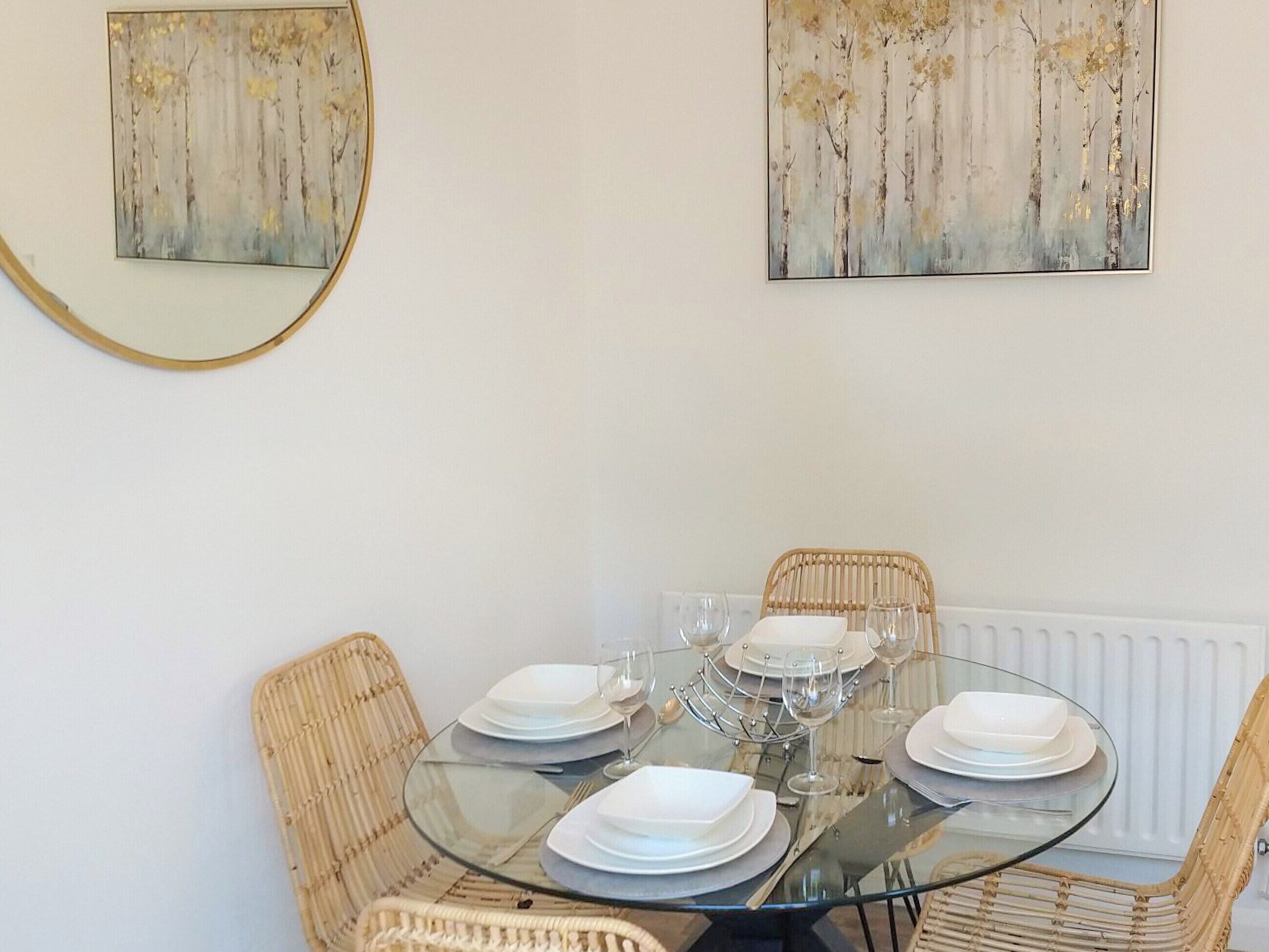 A dining area with a round glass table set for four, surrounded by wicker chairs.