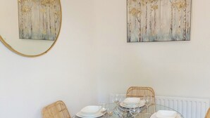 Un coin repas avec une table ronde en verre, dressée pour quatre personnes, entourée de chaises en osier.