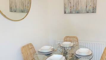 A dining area with a round glass table set for four, surrounded by wicker chairs.