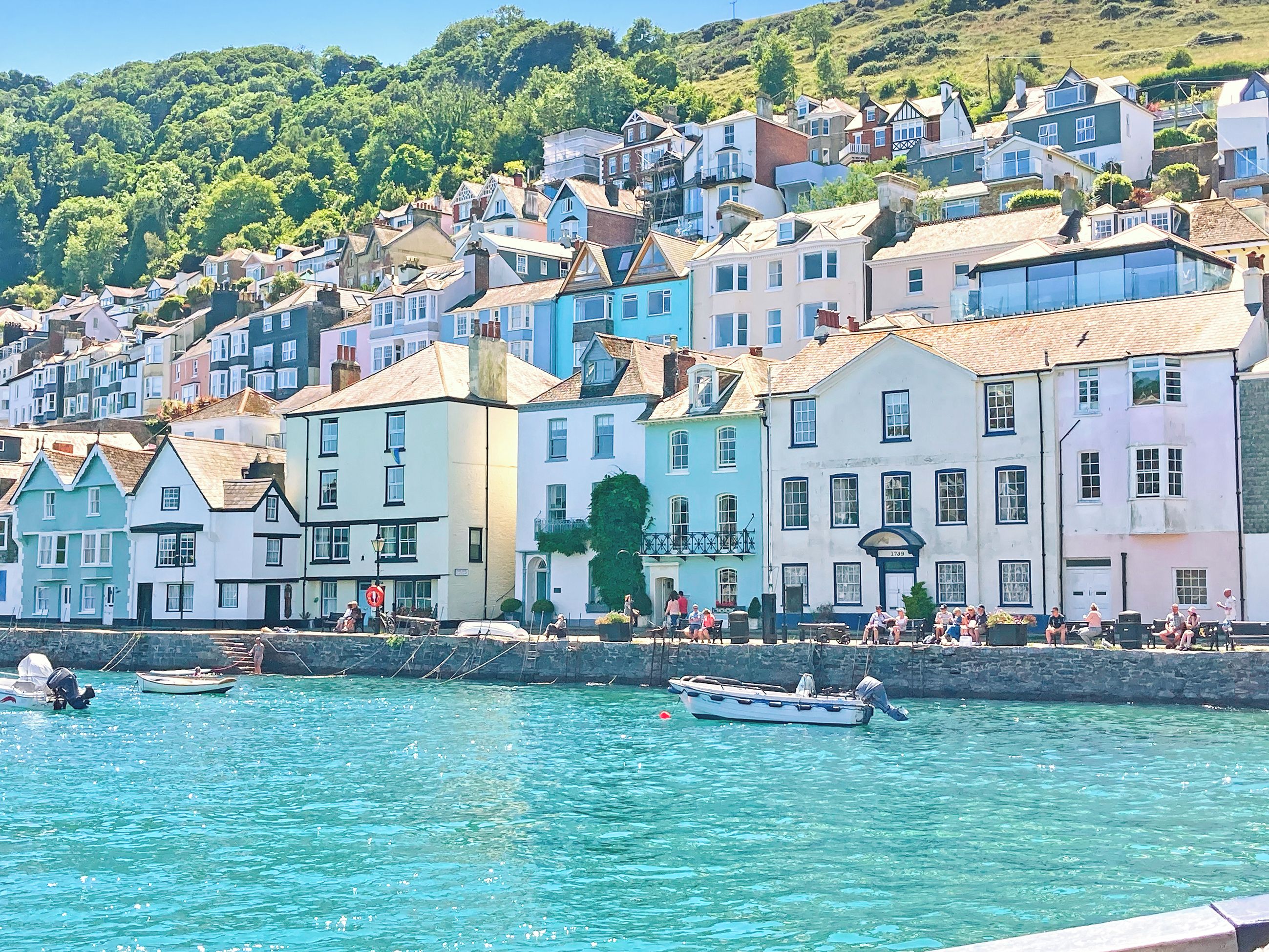 A coastal town with colorful buildings, a waterfront promenade, and a small boat docked near the shore.