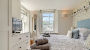 Een slaapkamer met een bed, een televisie, een dressoir, een spiegel en een raam met uitzicht.