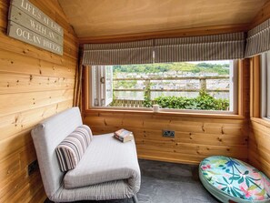 Ein Zimmer in einer Holzhütte mit einem Bett, einer Bank, einem Fenster mit Blick auf eine Stadt und einem Schild an der Wand.