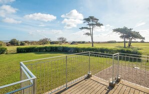 A view from a balcony with a metal railing, overlooking a grassy field with trees and a clear sky. - 4 bedroom accommodation in Thorpeness (Thorpeness)