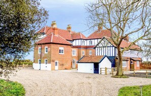 A traditional half-timbered house with multiple chimneys, a gravel driveway, and a large tree in the foreground. - 4 bedroom accommodation in Thorpeness (Thorpeness)