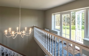 A staircase with a white balustrade leading to a landing with a chandelier. - 4 bedroom accommodation in Thorpeness (Thorpeness)