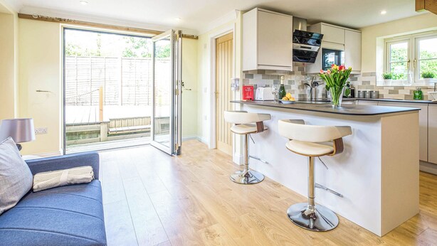A modern kitchen with a central island, bar stools, and a sliding glass door leading to a patio. - A romantic bolt hole near famous Aldeburgh on the Suffolk Heritage Coast. (Aldringham)