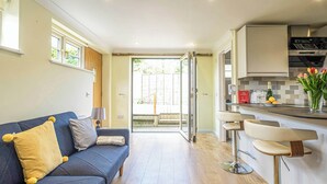 A modern kitchen with a bar area, a blue sofa with yellow and gray cushions, and a view to the outside. - A romantic bolt hole near famous Aldeburgh on the Suffolk Heritage Coast. (Aldringham)