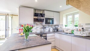 A modern kitchen with white cabinets, a large island, a microwave, and a window. - A romantic bolt hole near famous Aldeburgh on the Suffolk Heritage Coast. (Aldringham)