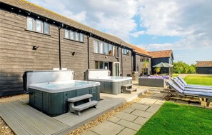 A modern outdoor hot tub area with a wooden deck, lounge chairs, and a barbecue grill. - 7 bedroom accommodation in Darsham, near Saxmundham (Darsham, near Saxmundham)