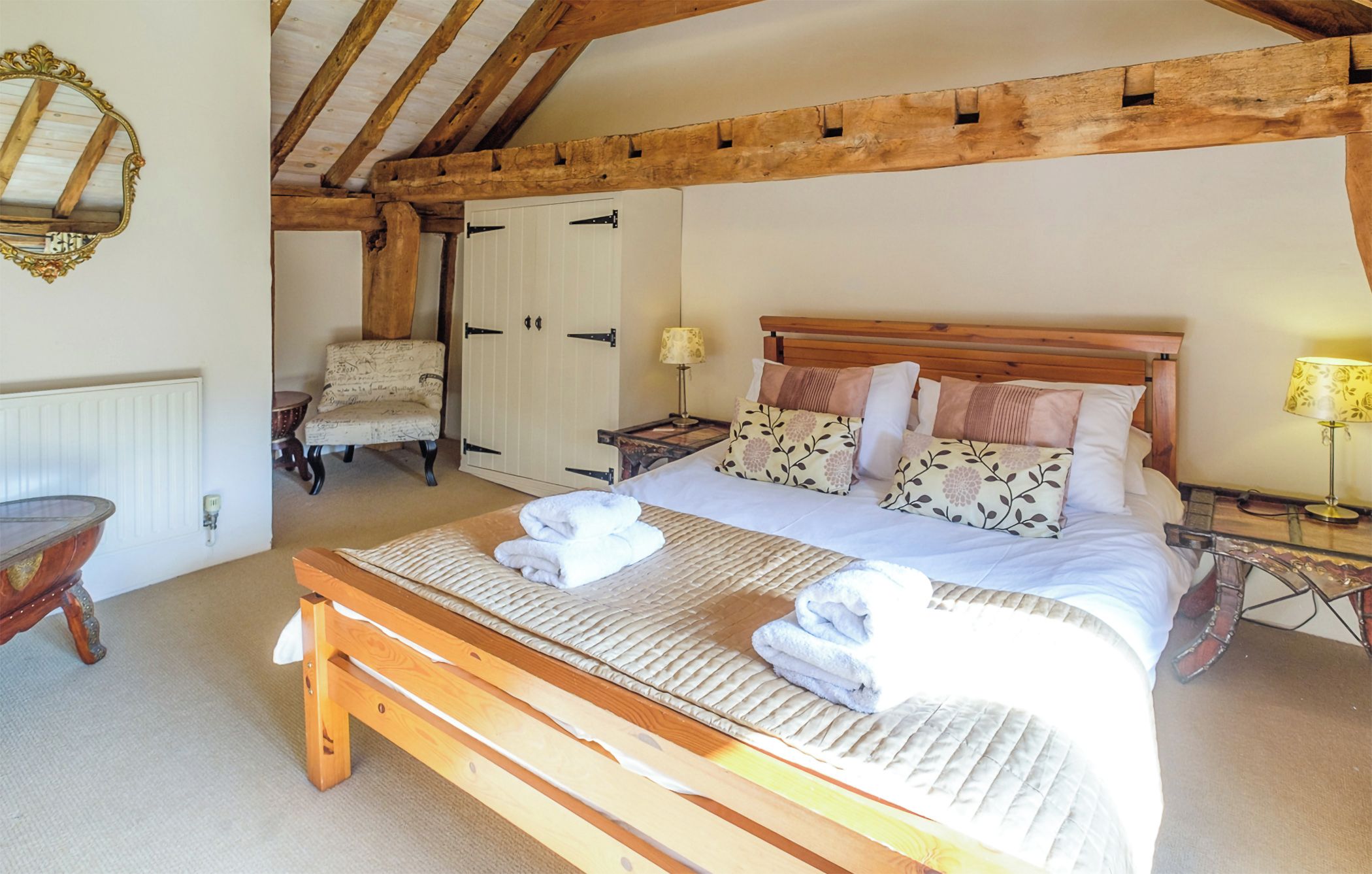 A bedroom with a wooden bed, a bench, a chair, a bedside table, and a wardrobe.