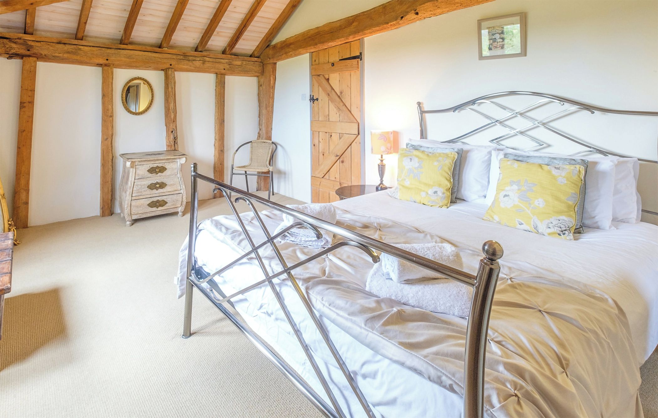 A bedroom with a metal bed frame, a wooden door, a dresser, and a chair.