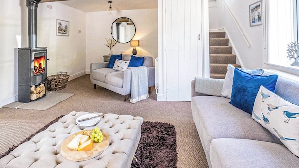 A cozy living room with a fireplace, sofas, a dining table with a fruit platter, and a staircase. - 2 bedroom accommodation in Blyford, near Halesworth (Blyford, near Halesworth)