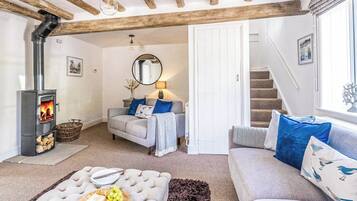 A cozy living room with a fireplace, sofas, a dining table with a fruit platter, and a staircase.