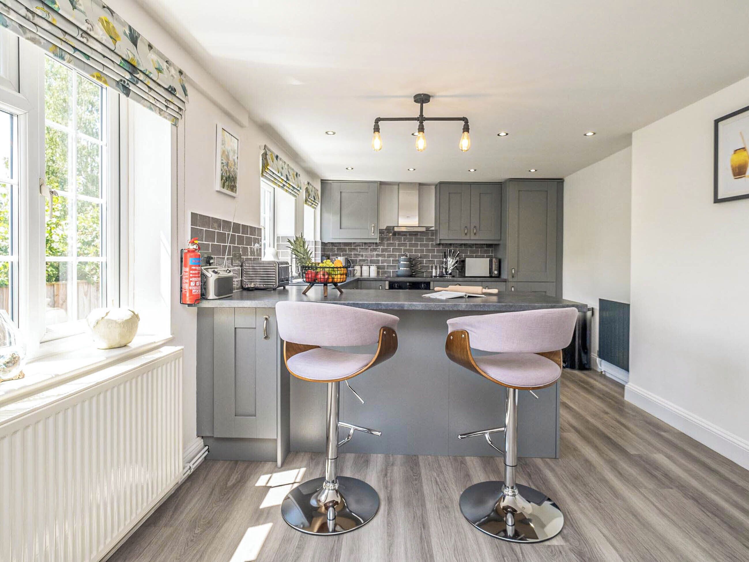 A modern kitchen with grey cabinets, a central island with bar stools, and a window with a view of greenery.