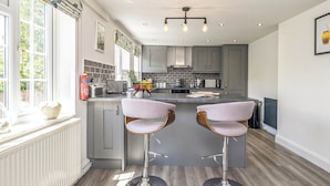 A modern kitchen with grey cabinets, a central island with bar stools, and a window with a view of greenery. - 2 bedroom accommodation in Blyford, near Halesworth (Blyford, near Halesworth)