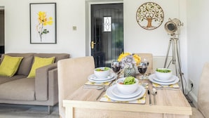 A dining area with a wooden table set for four, surrounded by a sofa and a chair. - 2 bedroom accommodation in Blyford, near Halesworth (Blyford, near Halesworth)
