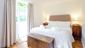 Un dormitorio con cama, lámparas de noche, un banco de madera y una ventana con cortinas.