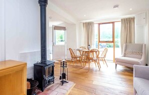 Een gezellige woonkamer met een houtkachel, een eethoek met houten stoelen en een bank.
