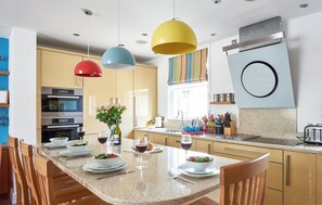 Een moderne keuken met een centraal eiland, roestvrijstalen apparatuur en kleurrijke hanglampen.