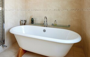 A modern bathroom with a freestanding bathtub, a glass shelf with toiletries, and a towel rack. - 2 bedroom accommodation in Aldeburgh (Aldeburgh)