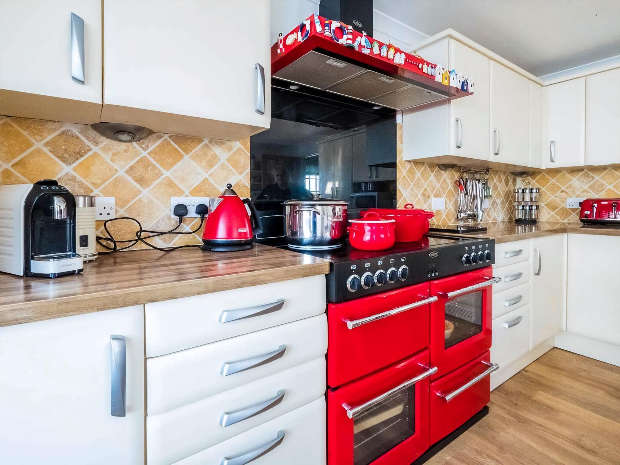 Una cocina con armarios blancos, una estufa roja y una cafetera.