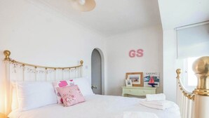 A bedroom with a white bed, a small bedside table, a framed picture, and a sign with the letters "GS" on the wall. - 2 bedroom accommodation in Aldeburgh (Aldeburgh)