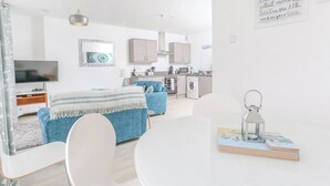 Ein modernes, helles Schlafzimmer mit Bett, Fernseher und einer Küche im Hintergrund.